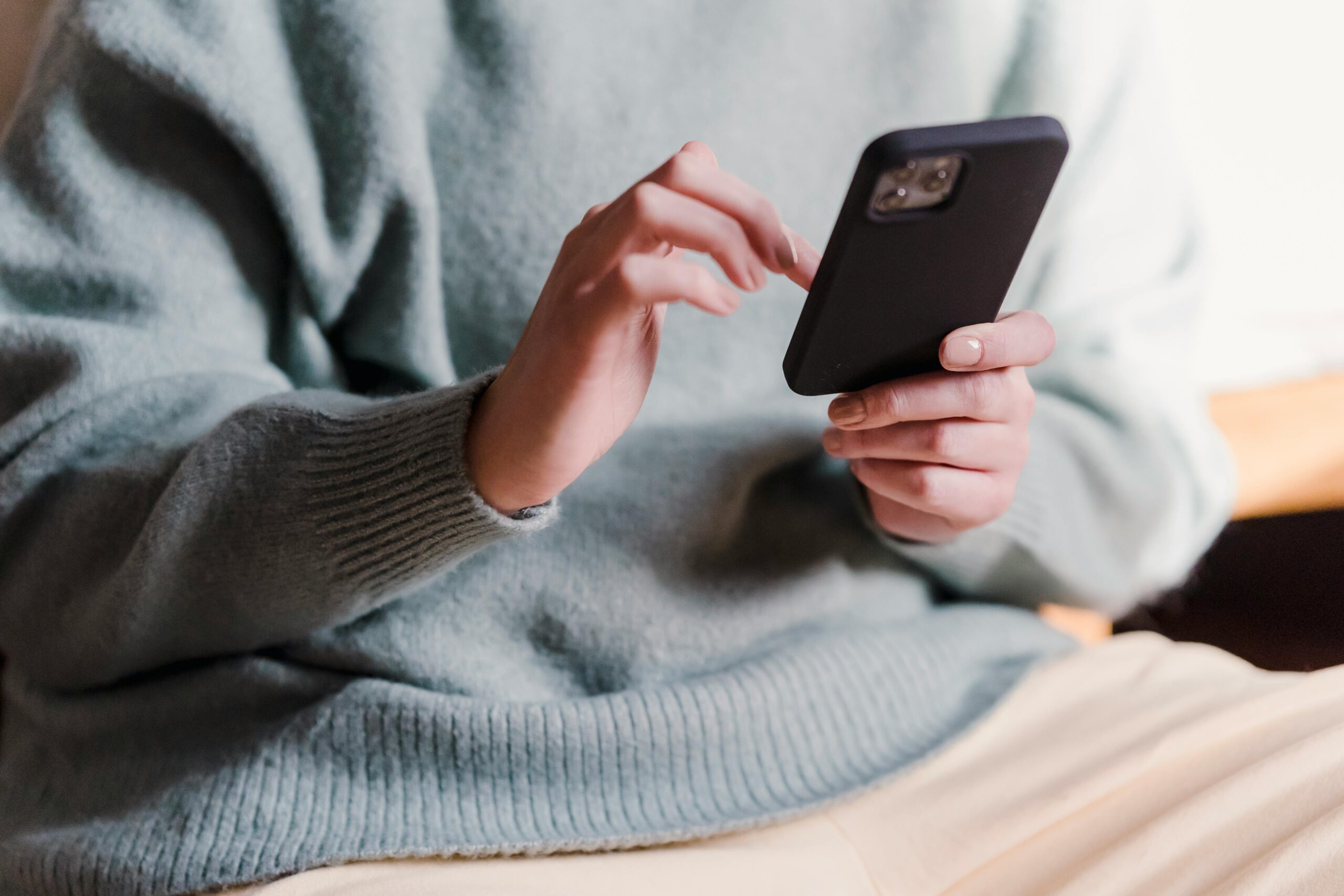 Crop faceless female in casual clothes using smartphone and touching screen while chilling at home